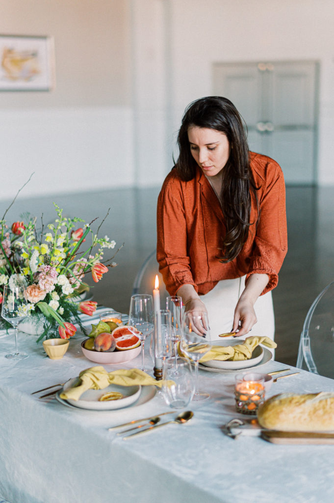 A young female wedding planner setting a table with tableware and silverware